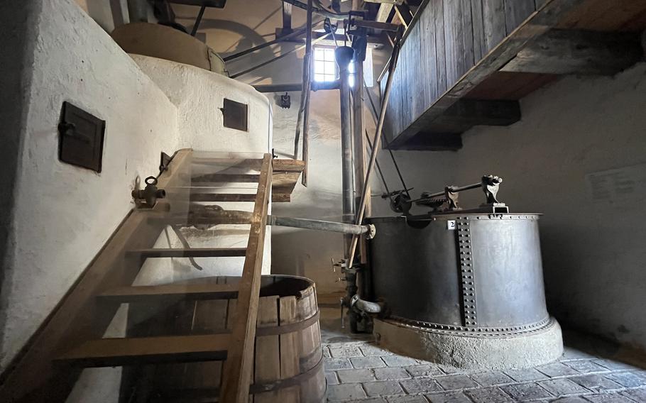 Interior of a historic mill showing large wooden gears, grinding stones, a wooden barrel and traditional milling equipment with exposed wooden beams overhead.