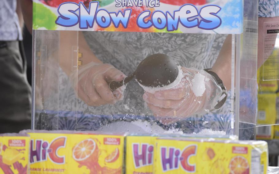 A close-up view of a pair of hands behind a clear glass partition scooping shaved ice into a cup for a snow cone.