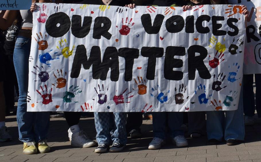 A large poster reading “Our voices matter” is held by DODEA students, with only their legs and hands visible. 