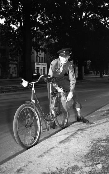 A vertical black and white photo of a service member behind a bicycle.