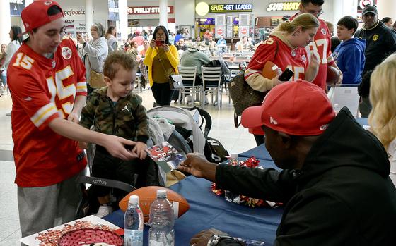 Christian Okoye, right, hands a signed photo to Kaden Moore, center left, and Noah Kees, right, during an event with the Kansas City Chiefs on Nov. 2, 2023, at the exchange at Ramstein Air Base, Germany. Okoye played for the Chiefs from 1987 to 1992.