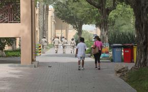 A boy and a woman walk together in Bahrain with service members in the background. 