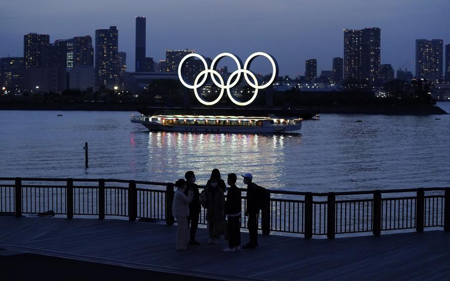 People watch illuminated Olympic rings floating in the waters off Odaiba island in Tokyo on April 1, 2021. 