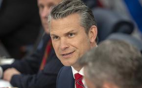 Pete Hegseth smiling as he speaks between two out-of-focus heads.