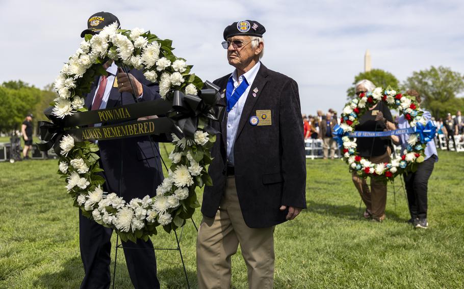People in groups of two carry large memorial wreaths across a grass field.