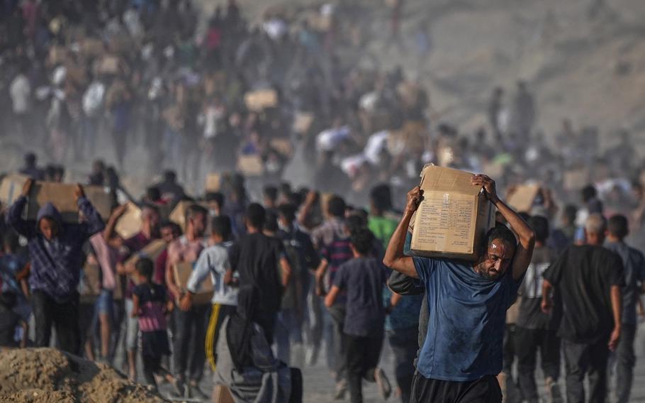 A crowd of people walks and carries boxes of aid.