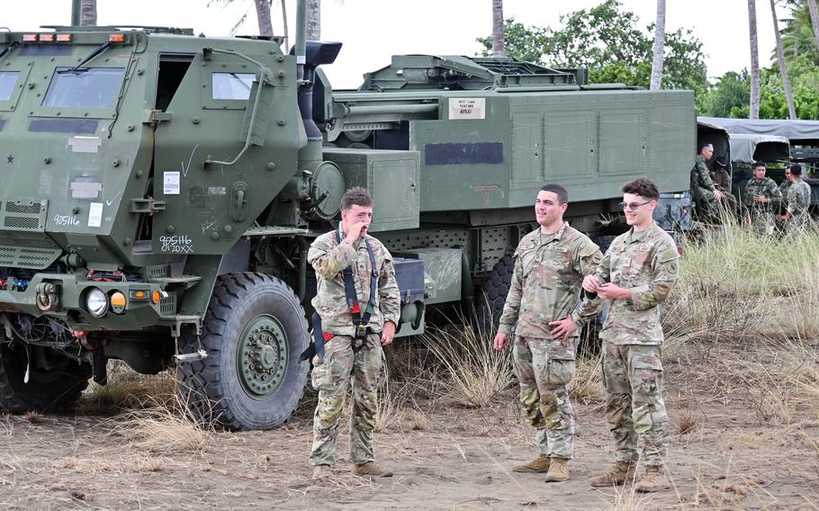 U.S. soldiers stand in front of a military vehicle.