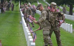 Members of the 3rd Infantry Regiment, also known as The Old Guard, place flags on a row in section 12 of Arlington National Cemetery on Thursday, May 23, 2024, to honor service members for Memorial Day.  