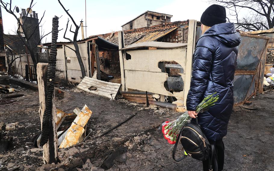 A woman with flowers stands by the house of Olha and Hryhorii Putiatin and their three children who died in a fire caused by a Russian drone attack on the oil depot at night on Feb. 10, 2024, in Kharkiv, northeastern Ukraine.