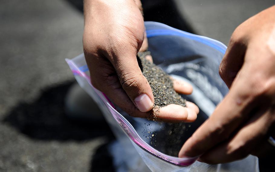 A U.S. airman from Kadena Air Base, Okinawa, collects black volcanic sand during a tour of Iwo Jima, also known as Iwo To, July 26, 2012.