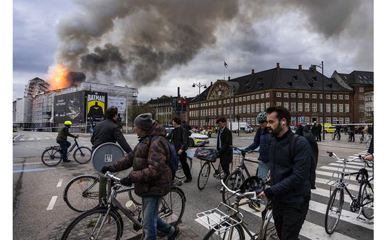 People ride bicycles as smoke rises from the Old Stock Exchange in Copenhagen, Denmark, Tuesday, April 16, 2024. A fire raged through one of Copenhagen’s oldest buildings on Tuesday, causing the collapse of the iconic spire of the 17th-century Old Stock Exchange as passersby rushed to help emergency services save priceless paintings and other valuables. (Emil Nicolai Helms/Ritzau Scanpix via AP)
