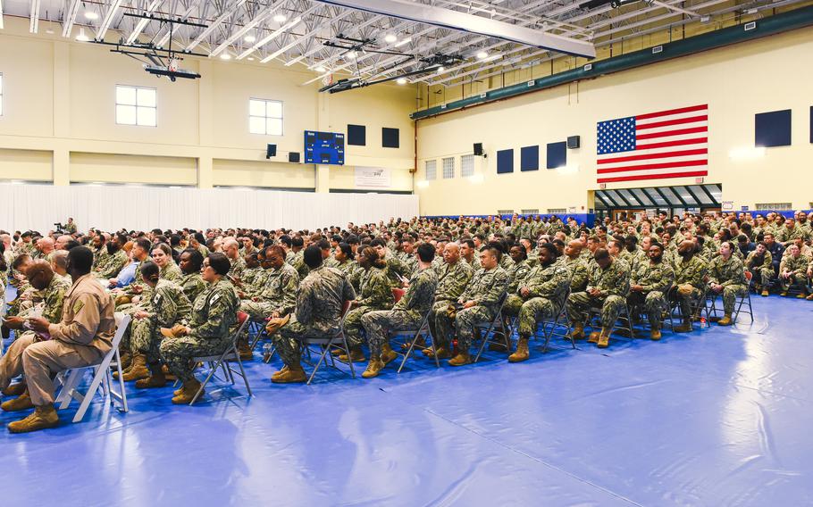 Marines and sailors seated in the auditorium with an American flag on the back wall.