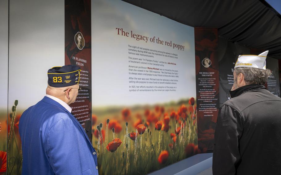Two older veterans wearing hats from their service look on at a display.