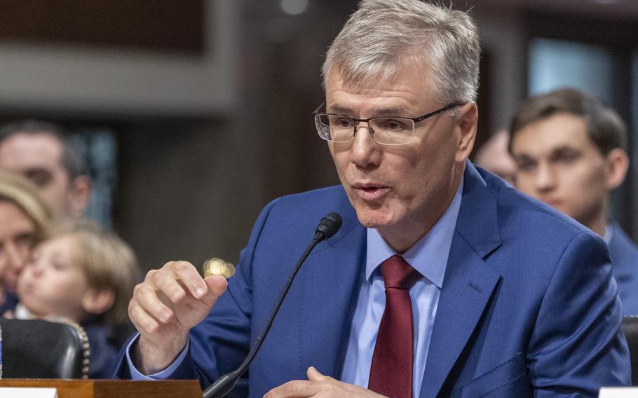 A man in glasses and a blue suit speaks into a microphone while seated at the witness table in a congressional hearing room.
