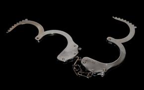 A pair of open handcuffs laid against a black background.