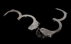A pair of open handcuffs laid against a black background.