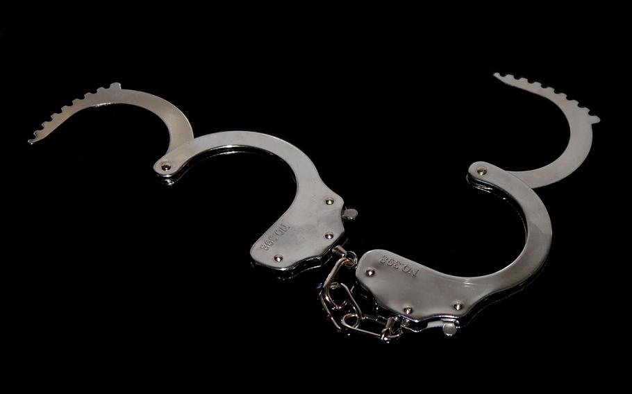 A pair of open handcuffs laid against a black background.