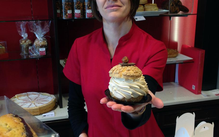 A sales clerk at Patisserie Rebert in Wissembourg, France, holds up a caramel cream puff, a sublime confection of whipped cream, toffee bits and caramel sauce sandwiched between two pastries.

