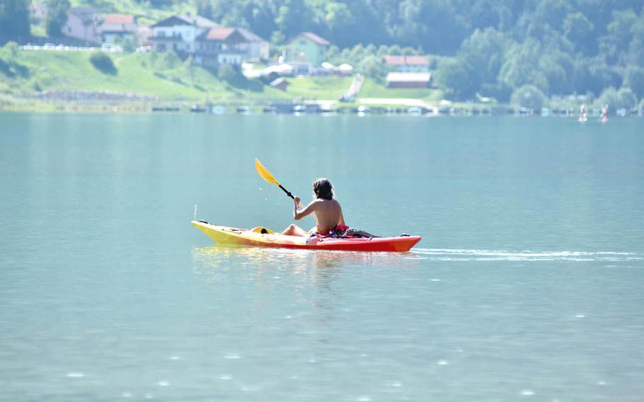 A man paddles a kayak on Italy's Lago di Santa Croce. The town of Farra D'Alpago in the background.