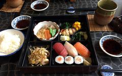 A lunch bento box from pre-pandemic times at Hashimoto in Saarbruecken, Germany. The meal includes sushi, grilled fish, vegetables, pickles, rice and green tea.

