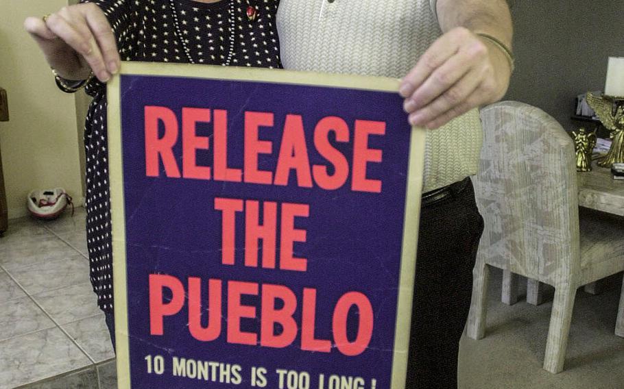 In a February, 2000 photo, Pueblo survivor James Kell and his wife, Pat, hold up a sign from 1968.