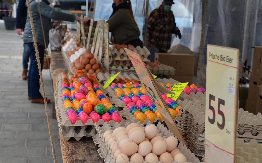 A woman pays for eggs at a stand in the outdoor market in Kaiserslautern, Germany, on Tues., April 6, 2021. The colorful eggs in the foreground are hard-boiled eggs from free-range chickens fed only organic foods.