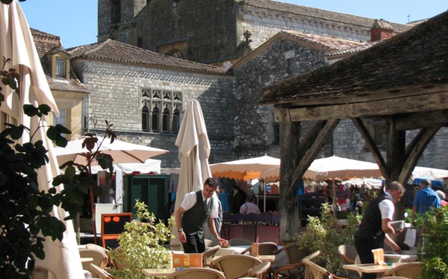 On a brilliant day in Monpazier, France, waiters prepare tables in anticipation of a sun-seeking lunch crowd on Place des Cornières.
