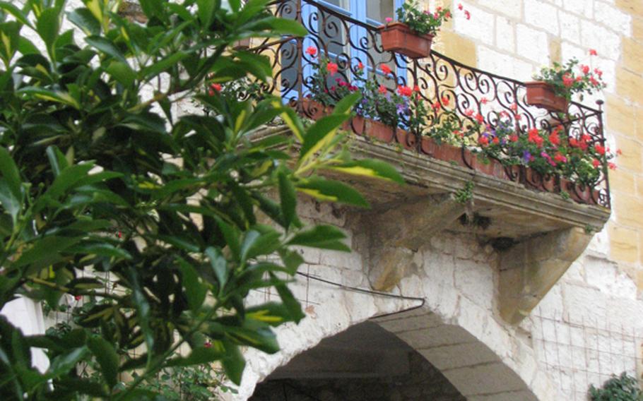 Bright geraniums enhance the iron balcony above a graceful arch on Place des Cornières in medieval Monpazier, France.