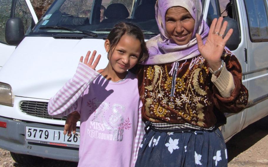 A pair of  Moroccans who fed and entertained a group of tourists when their van broke down, wave good-bye as the friends depart in a new vehicle, leaving the broken-down van behind.