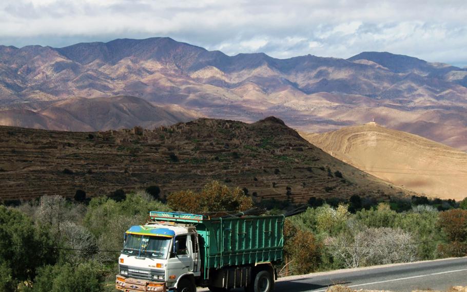 A slow-moving truck moves through the rippling hills of the Atlas Mountains in Morocco.