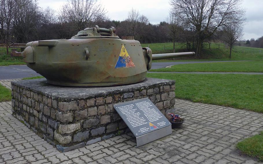 The turret of a Sherman tank, featuring the emblem of the 10th Armored Division, on road N874 on the outskirts of Bastogne, Belgium,  is pointed toward the Mardasson Monument.