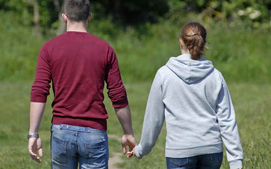 A young couple walks hand-in-hand through the meadows alongside the Main River in Hochheim am Main, Germany.