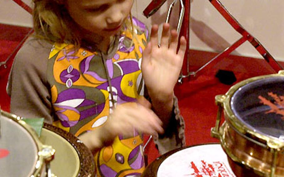 A young girl beats out a rhythm on a drum set.