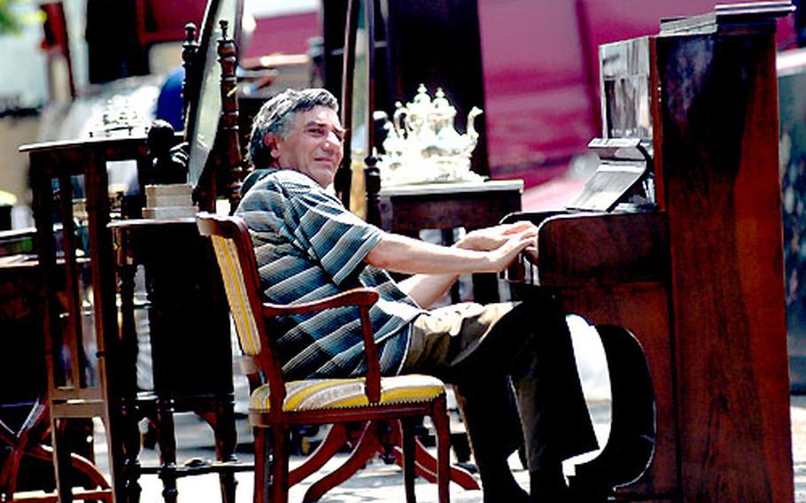 A Naples vendor plays an antique piano at an outdoor market to attract customers on a sweltering Saturday.