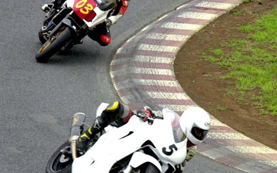 A couple of motorcyclists lean into a turn at the Tsukuba Circuit.
