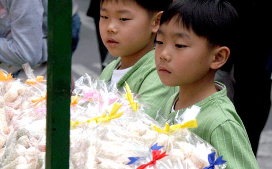 Boys watch a man prepare a type of sesame brittle. He gave them each a piece after he finished cutting the slab by hand.