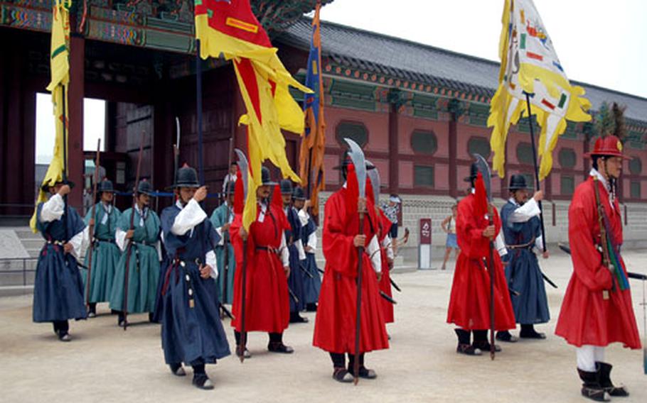 Guards at Gyeongbokgung Palace march out of the main gate as part of a changeover ceremony. The various costumes denote different jobs for each man: the ones in green are guards; the ones in red robes with black hats, military band members; and the ones in blue are time messengers.
