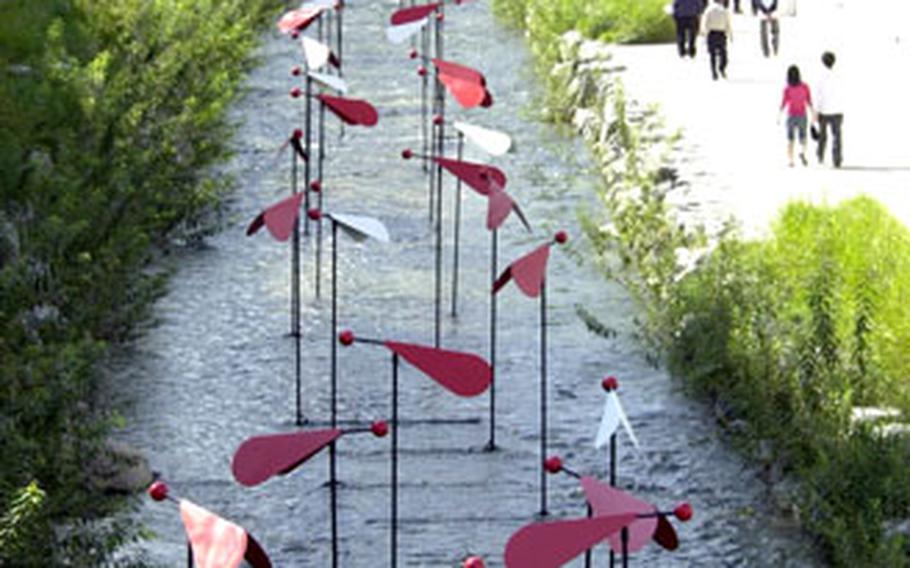 A series of red and white artwork stands in the center of Cheonggye Stream.