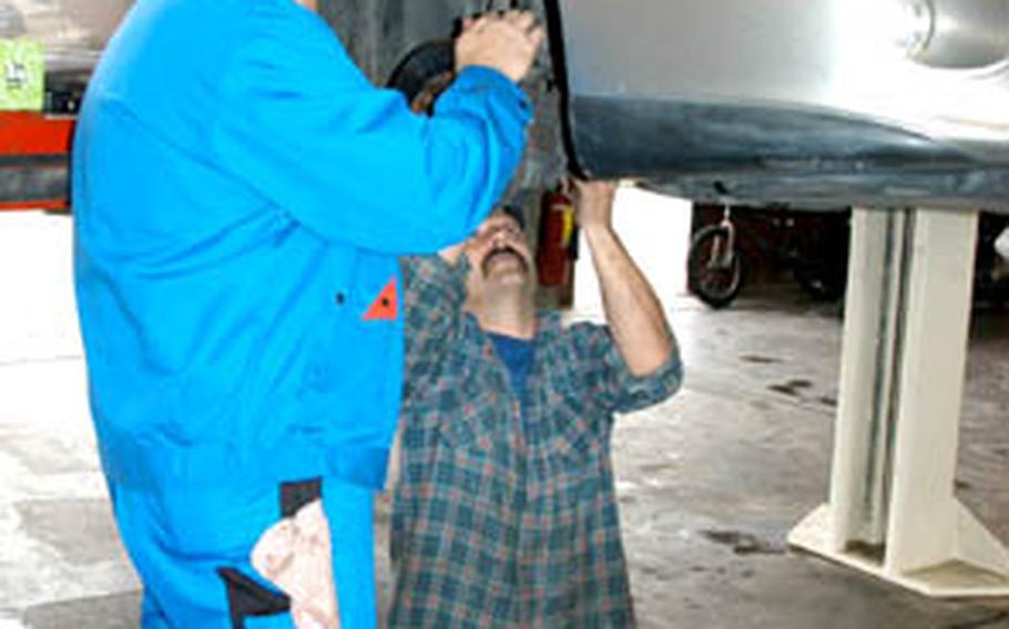 Scott Helgelien, left, a mechanic from the Warner Barracks Auto Skills shop in Bamberg, helps Jim Willis, kneeling, work on his car last month. The shop is a popular weekend place for amateur and professional mechanics to do repairs and maintenance on their cars.