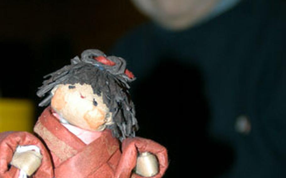 Eiko Ohyama inspects one of her many washi creations. The dolls often are adorned with accessories. This girl holds a mari ball.