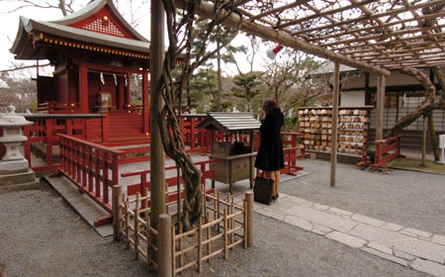 A Japanese woman pays respects by tossing money and praying at a Hachimangu shrine in Kamakura. The Hachimangu shrine is dedicated to the memory of samurai and has many events held at it each year. The main halls act also as a museum, and the ponds and parks are open to the public.