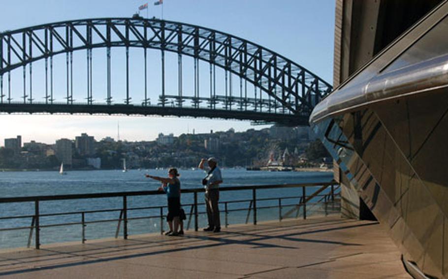 Standing near two of the city’s landmarks — the Opera House, right, and harbour bridge — tourists point toward the downtown area.