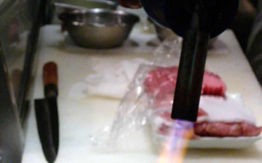A Japanese sushi chef prepares abute toro with a blow torch at his station in a restaurant in Tokyo.