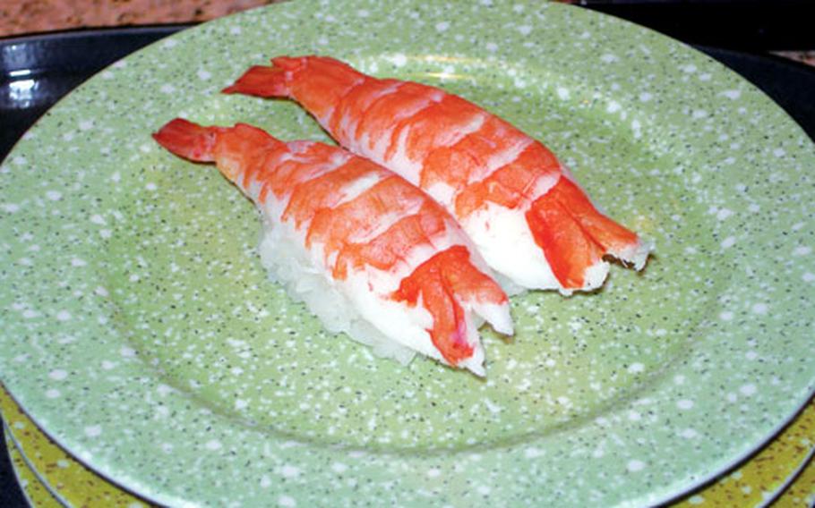 Ebi, or shrimp sushi. is placed on a green plate to signify the cost of the dish.