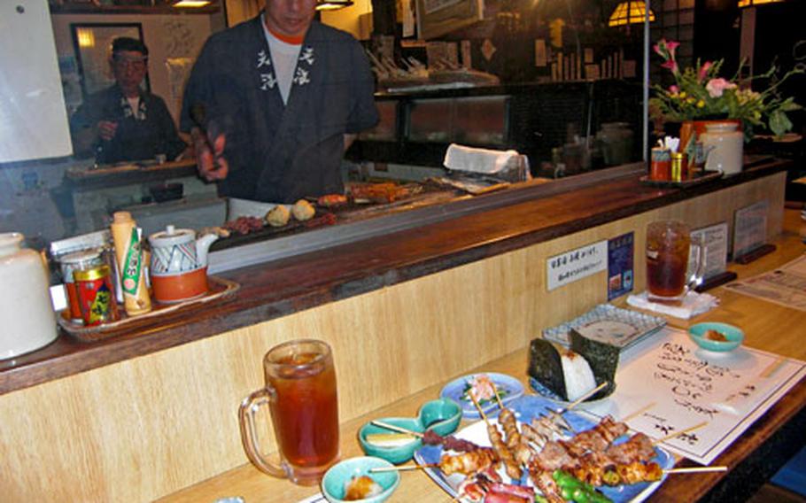Yakitori chef Kanji Sugimura, front, intently tends pork ribs and chicken meatballs on the grill as the owner, Kenzo Kanamori, waits to serve them to his hungry diners at Yakitori Tenkai in Chatan, Okinawa.