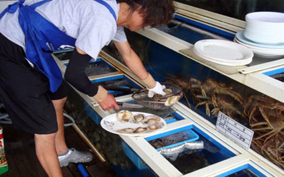 A server at Seoul Hoe Chip halves scallops fresh out of the tank. A plate full of raw scallops that customers cook on a grill at their table costs 50,000 won, or about $40.