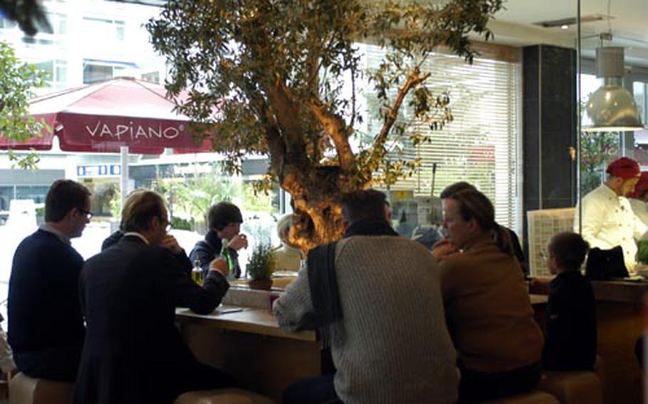 Guests enjoy a lunch at one of the larger tables at the Vapiano restaurant in Wiesbaden, Germany. Various stands within the restaurant allow the customer to choose from pizza, pasta, appetizers, desserts, salads or a favorite spirit, including a selection of 25 wines.