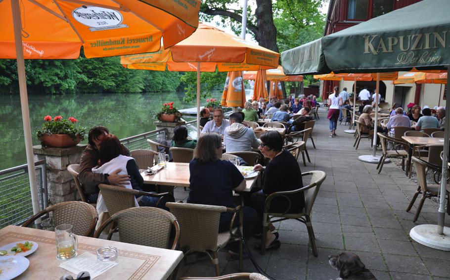 The beer garden and restaurant Bootshaus in Bamberg, Germany, offers a shaded seating area with a riverside view.