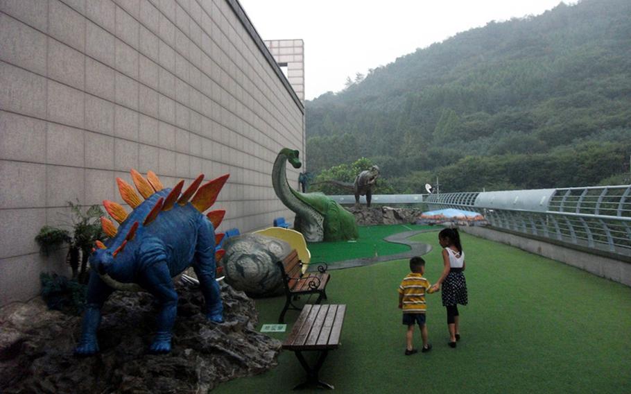 Natalya Jimenez takes her brother Diego through the Dinosaur Park despite some rain during a visit to Seoul's Seodaemun Museum of Natural History.