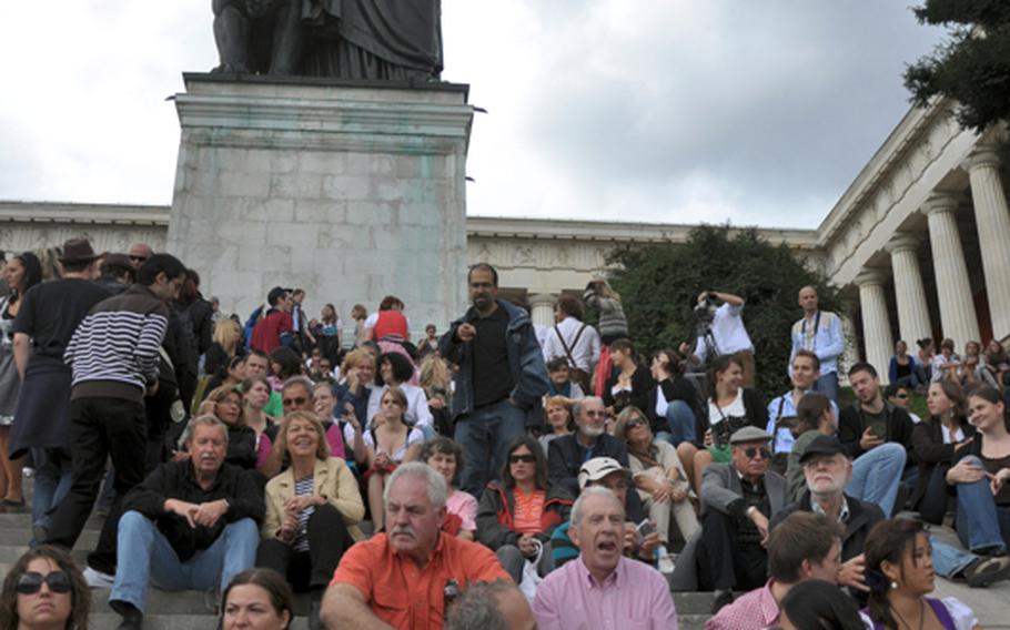 A statue of Bavaria stands over a crowd of people resting while at the 200th anniversary of Munich&#39;s Oktoberfest on opening day. The statue stands in front of the Hall of Fame on the edge of the festival grounds and depicts the state of Bavaria.